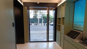 Un hall d’hôtel avec une porte vitrée donnant sur la rue, un comptoir de réception équipé d’un ordinateur et une vue sur la rue.