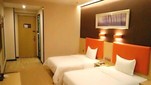 Ein Hotelzimmer mit zwei Betten, Holzboden, einem Bild an der Wand und einer Tür im Hintergrund.