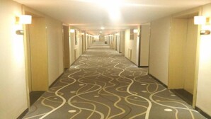 Ein Hotelgang mit einem gemusterten Teppich, Türen an beiden Seiten und Wandleuchten.