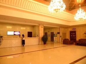 Un hall de hotel con mostrador de recepción, una planta grande en maceta y una zona de estar con sofás.