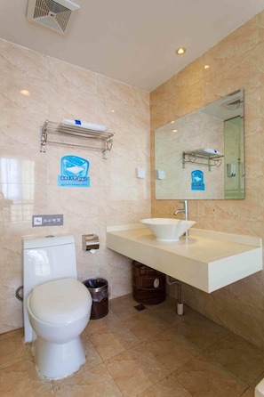 Une salle de bain avec des toilettes blanches, un lavabo surmonté d’un miroir et un porte-serviettes.