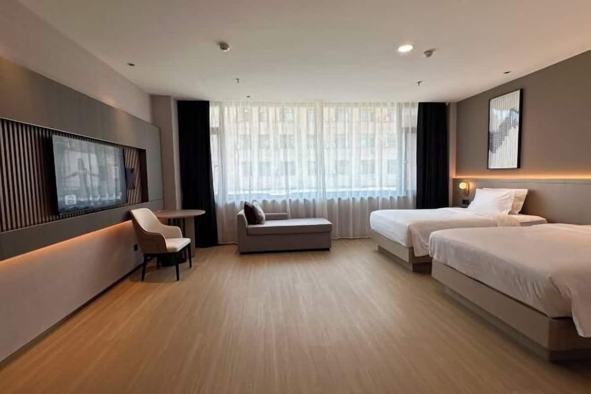 A hotel room with two beds, a sofa, a TV, and a window with curtains.