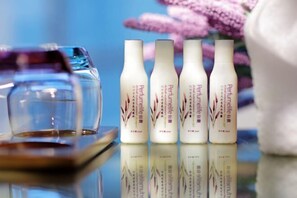 Four bottles of perfume on a reflective surface with a glass and a white cloth in the background. - Lavande Hotel (Zhuanghe Xiangyang Road) (Zhuanghe)