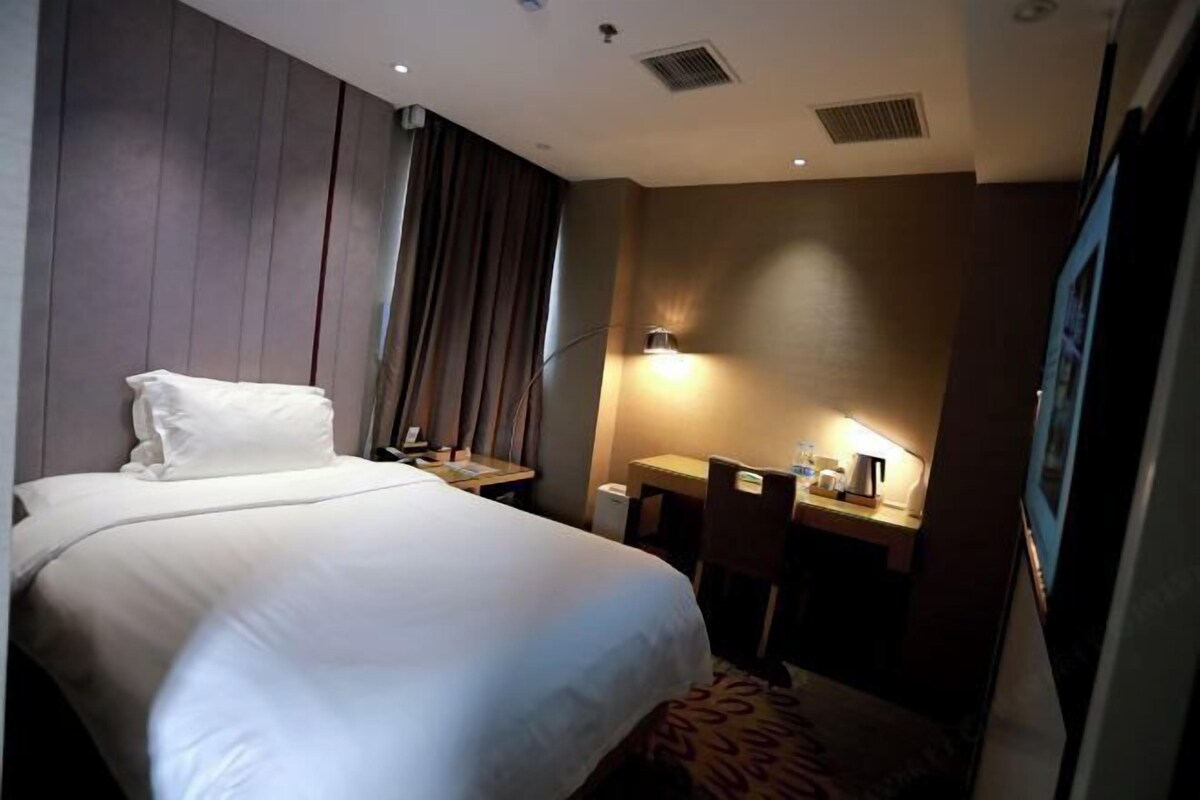 Ein Hotelzimmer mit einem großen Bett, einem Schreibtisch mit Stuhl, einer Lampe und einem Fenster mit Vorhängen.