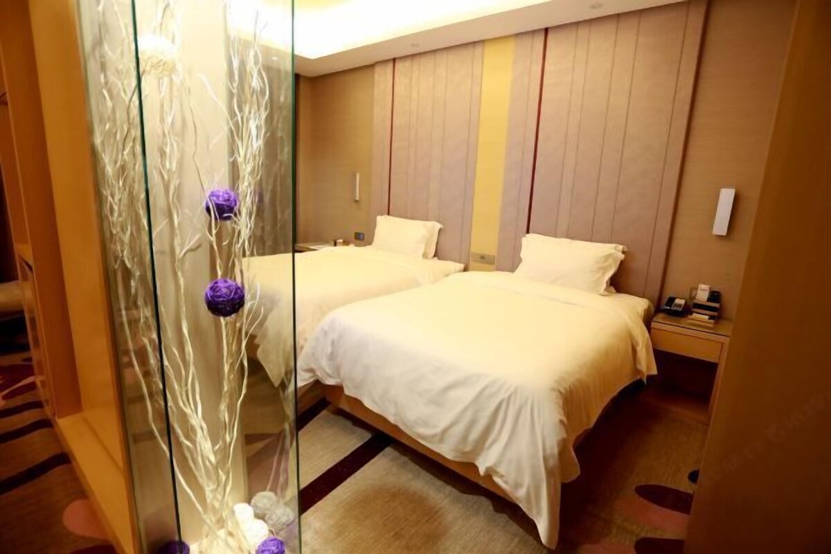 Ein Hotelzimmer mit zwei Betten, einer Glastrennwand und einer Zierpflanze.