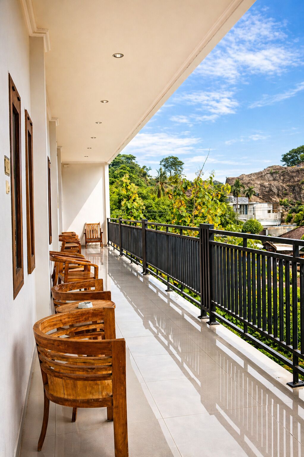Un balcón con sillas de madera y barandilla negra, con vista a un jardín exuberante y una ladera rocosa.