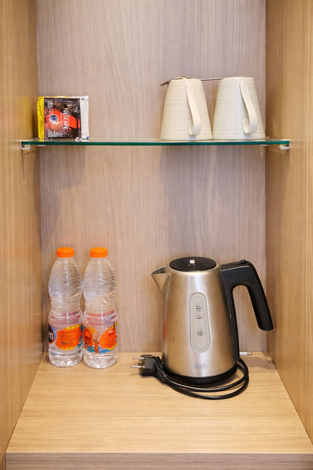 A kitchenette with a kettle, two water bottles, and a coffee maker on a shelf.