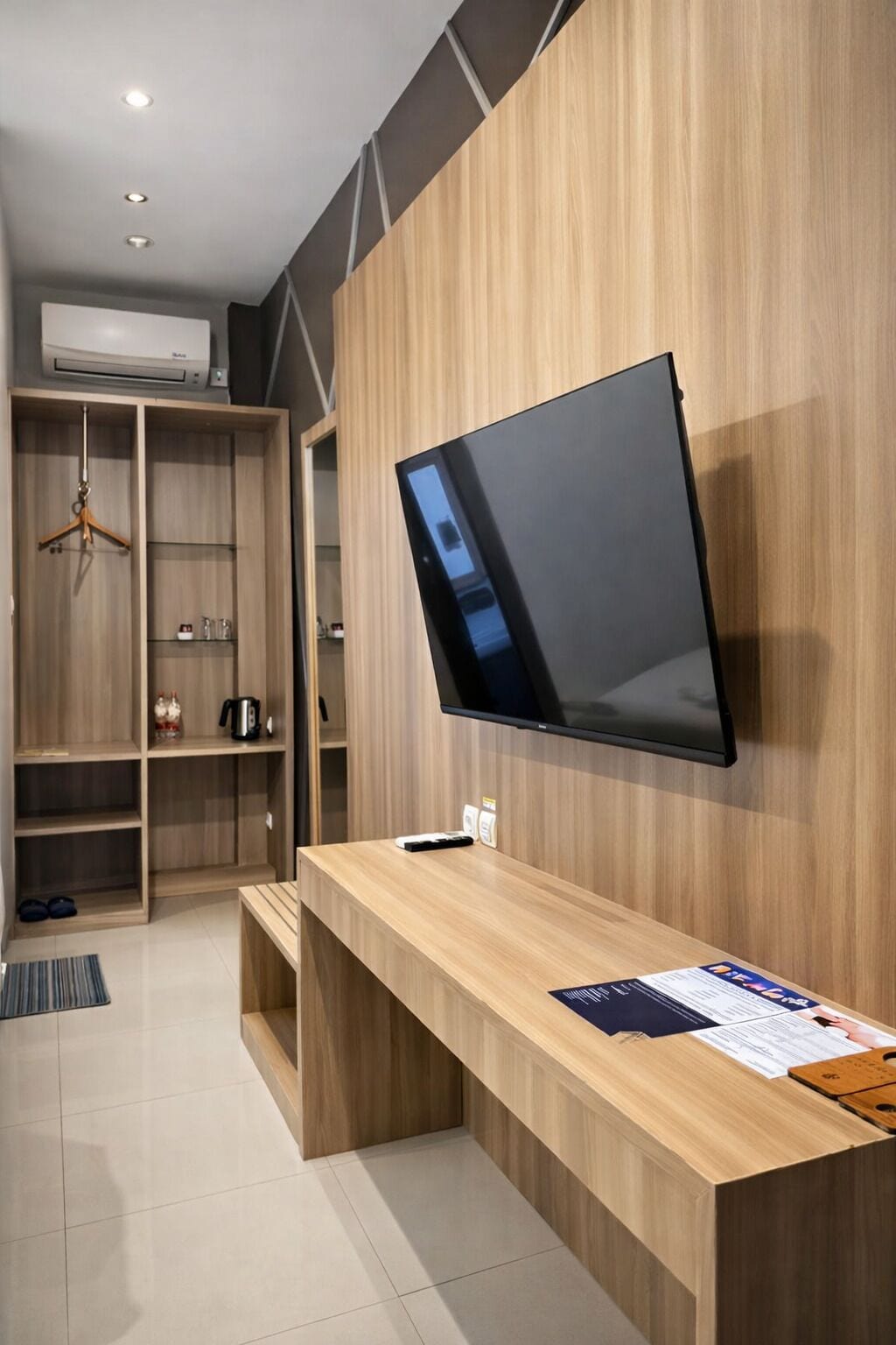 Una habitación moderna con un escritorio de madera integrado, un televisor de pantalla plana montado en la pared y un armario con estantes.