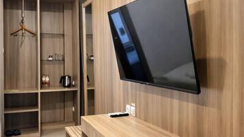 Una habitación moderna con un escritorio de madera integrado, un televisor de pantalla plana montado en la pared y un armario con estantes.