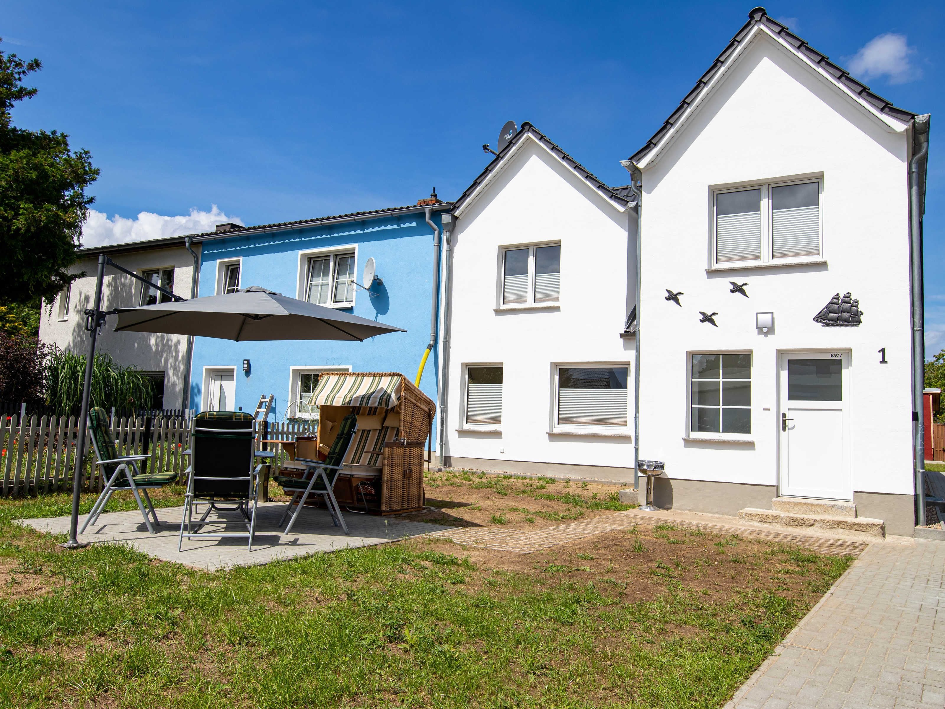 Ein zweigeschossiges Haus mit blauer Fassade, einer weißen Garage und einer Terrasse mit Gartenmöbeln.