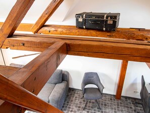 Un lit mezzanine en bois avec une valise posée dessus, une chaise grise et un sol carrelé.
