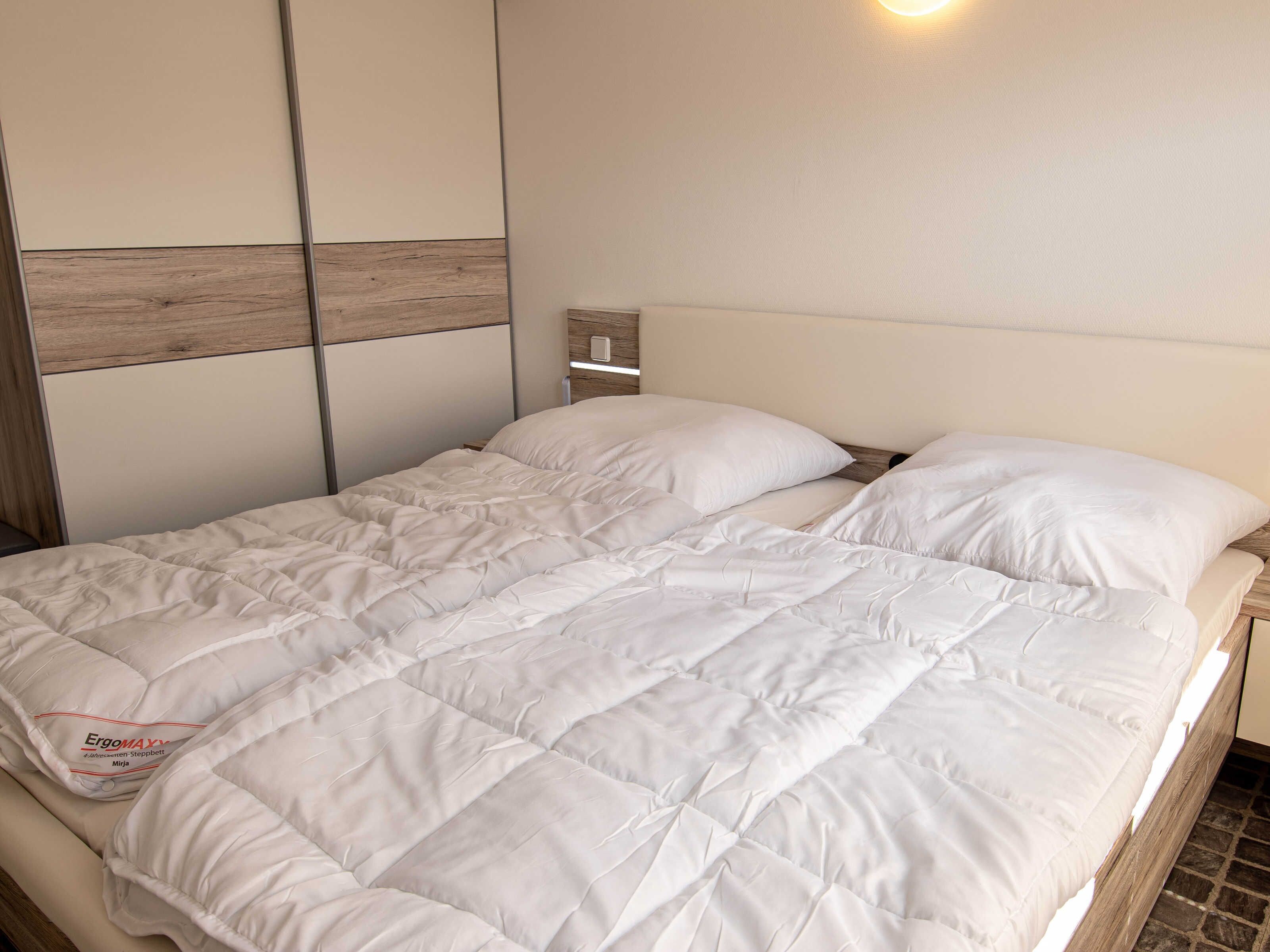 Ein Bett mit weißer Bettdecke, einem Holz-Kopfteil und einem Lichtschalter an der Wand.