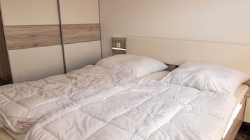 Ein Bett mit weißer Bettdecke, einem Holz-Kopfteil und einem Lichtschalter an der Wand.