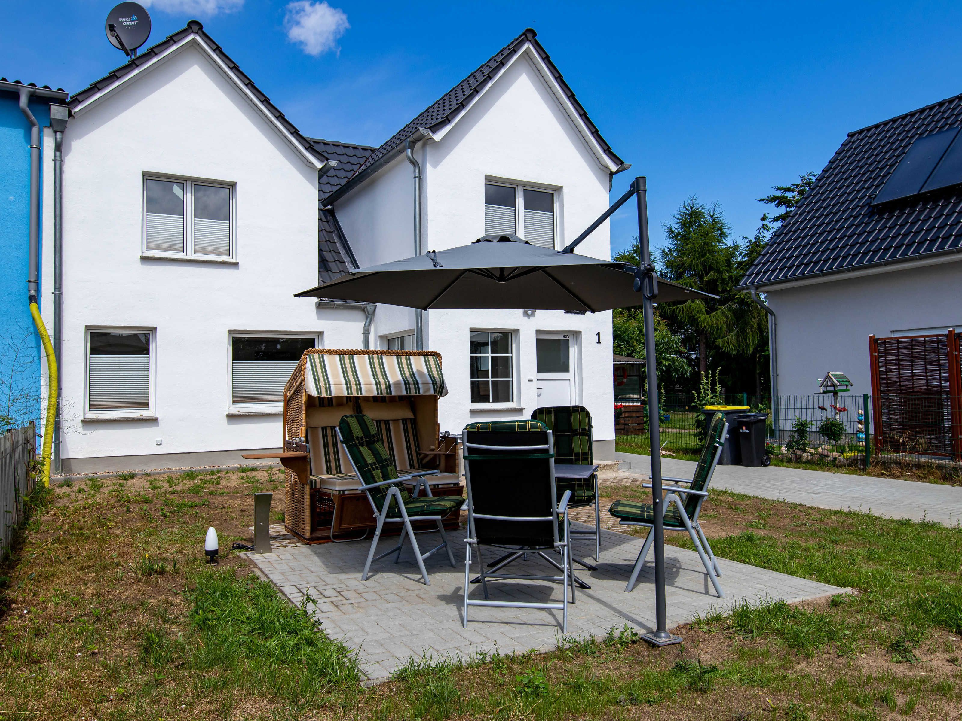 Une maison blanche dotée d’un patio aménagé avec du mobilier d’extérieur et un grand parasol.