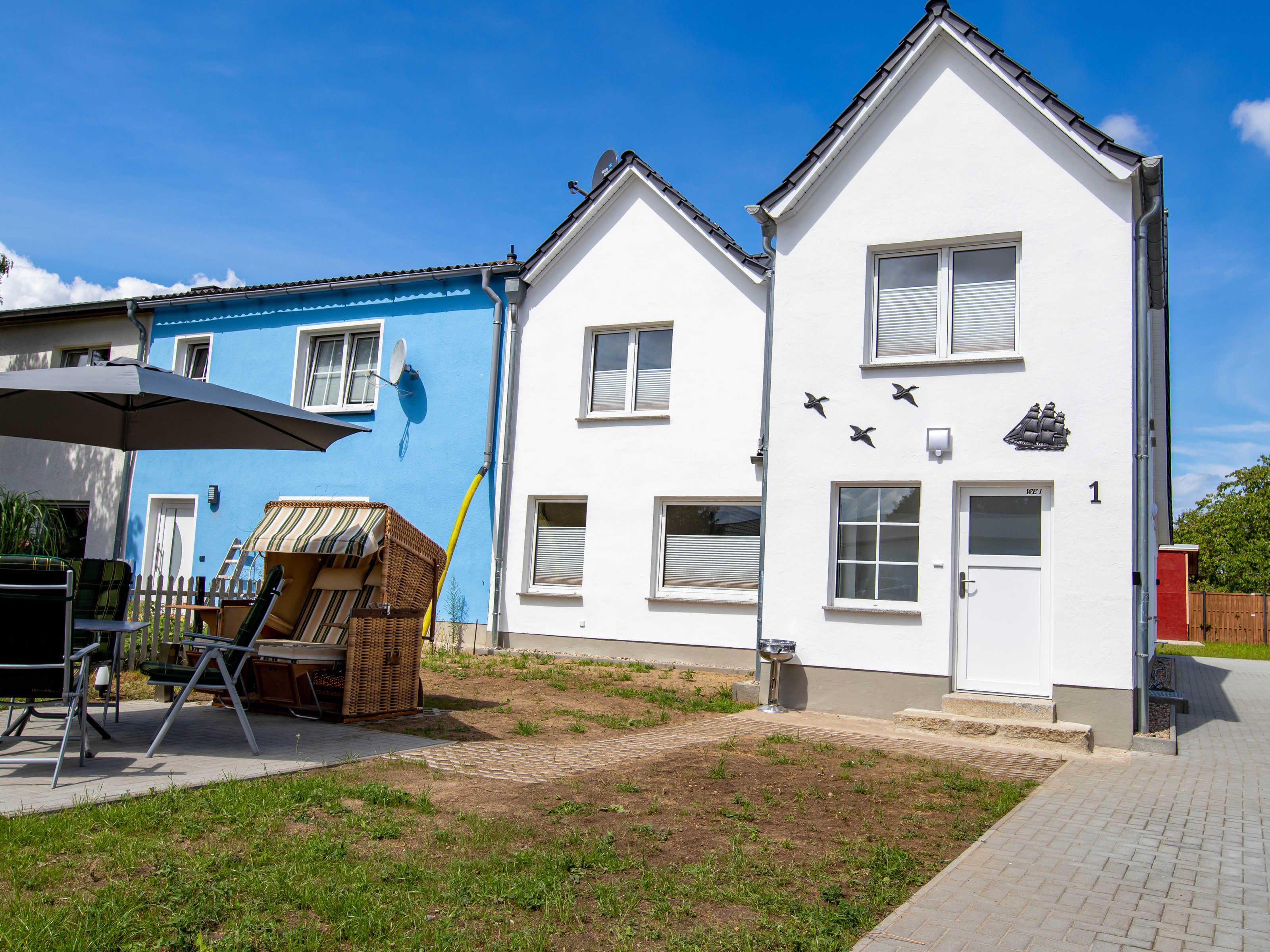 Ein zweistöckiges Haus mit weißer Fassade, einer blauen Tür und einem Schild mit der Nummer 1.