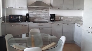 Una cocina moderna con una mesa de comedor de vidrio, armarios grises y una lámpara colgante roja.