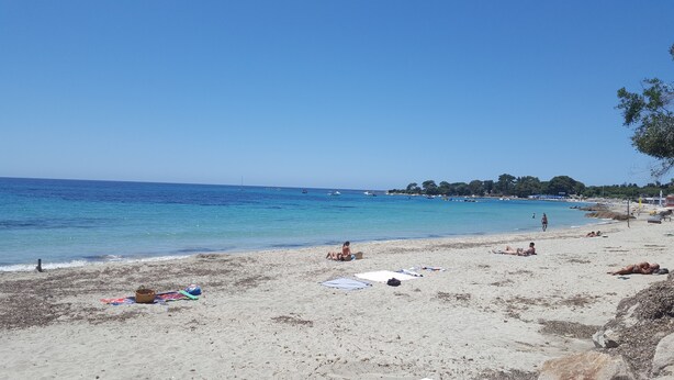 Una playa con agua cristalina, orilla de arena y algunas personas relajándose.