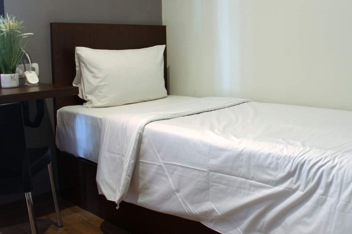 A neatly made bed with white linens, a wooden headboard, a bedside table with a lamp, and a small potted plant.