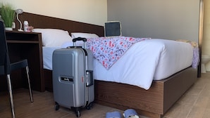 A neatly made bed with a floral blanket, a grey suitcase, and a pair of striped slippers on the floor. - Amarilis near Sam Poo Kong (Semarang)
