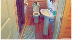 Een klein houten badkamertje met toilet, wastafel en raam.