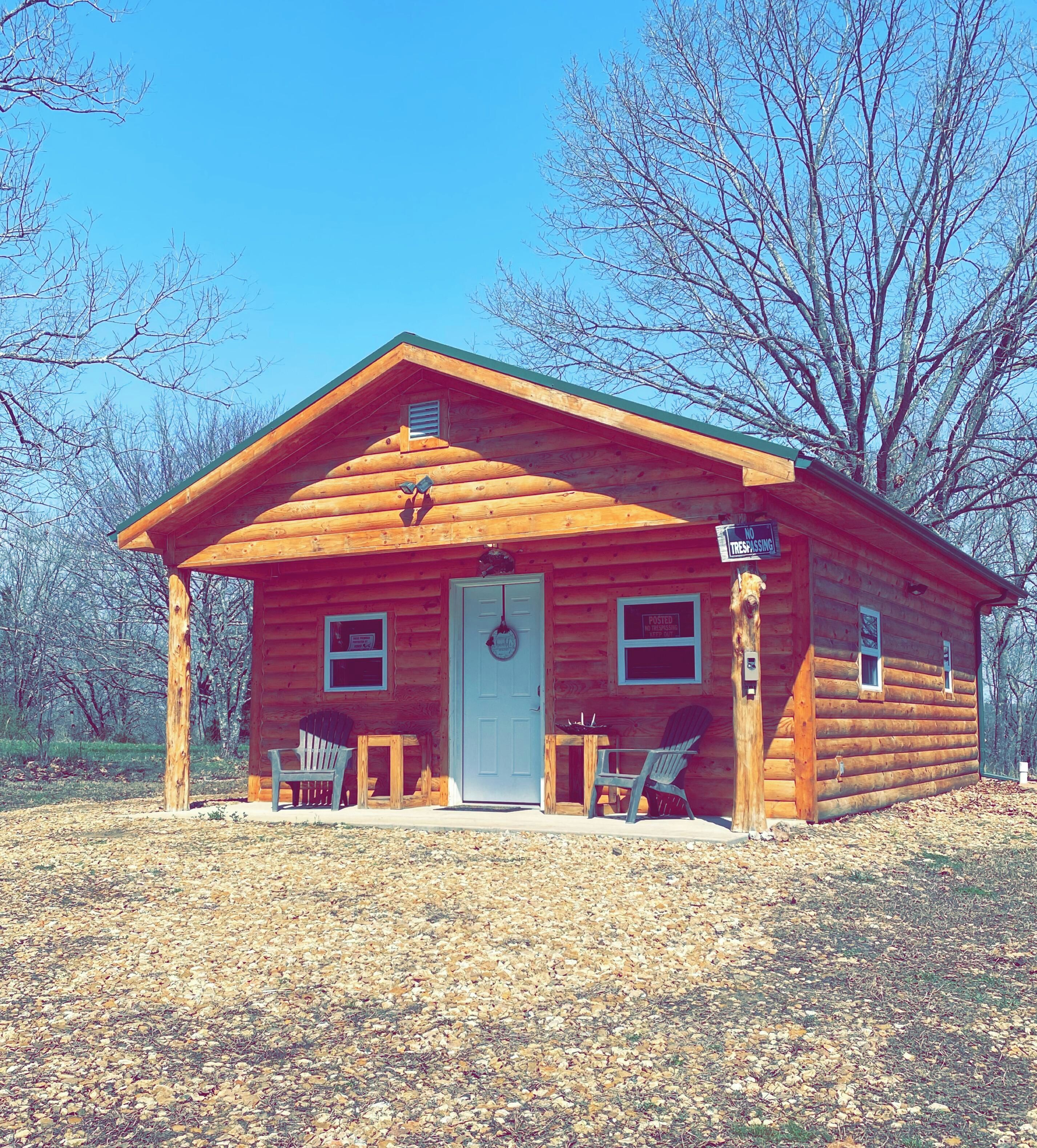 A log cabin with a front porch, two Adirondack chairs, and a mailbox.