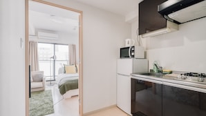 Cocina compacta con microondas, estufa y lavamanos. Se observa un pequeño comedor con una silla y una mesa.