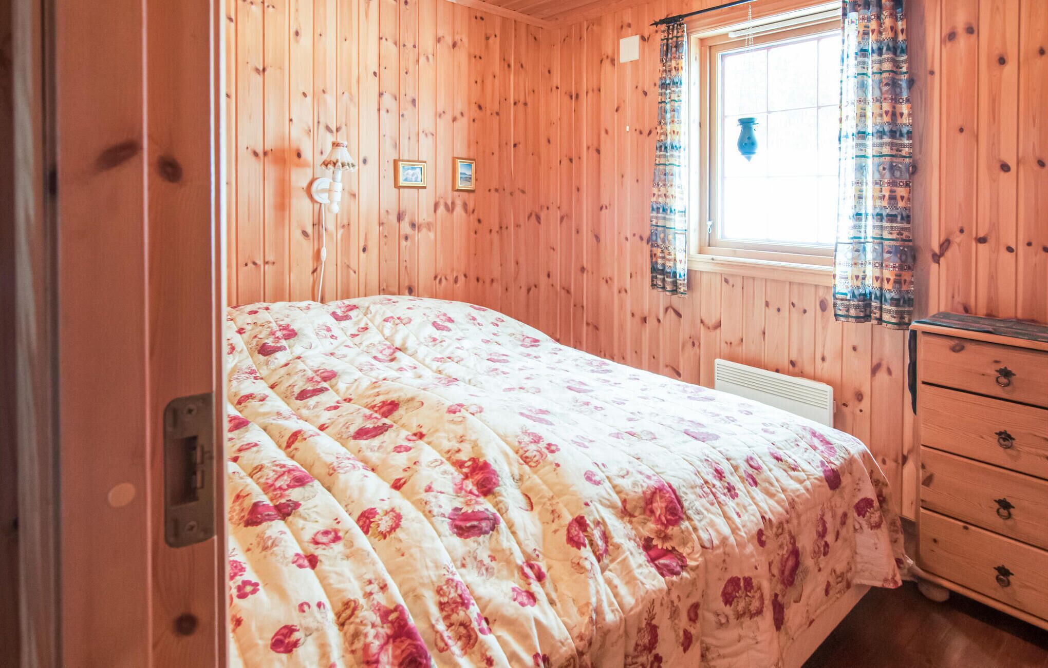 A wooden-paneled room with a bed, a dresser, and a window with patterned curtains.