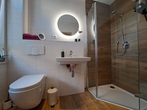 Un baño moderno con inodoro, lavamanos y ducha con mampara de vidrio.