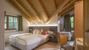 A bedroom with a bed, bedside table, lamp, and a small table with a chair. - Das kleine Hotel (Stumm)