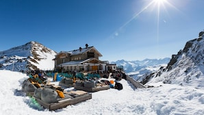 A mountain lodge with a wooden exterior, surrounded by snow-covered mountains and a clear sky. - Das kleine Hotel (Stumm)