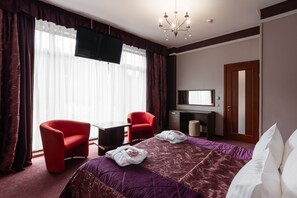 A hotel room with a large bed, a desk, a TV, and two red chairs. - VIP-Aparts Bukovel (Bukovel)