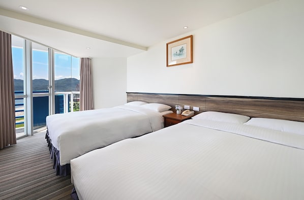 A hotel room with two beds, a wooden headboard, a nightstand with a phone, and a large window with a view of the mountains. - CT Green Bay Hot-Spring Hotel (New Taipei City)