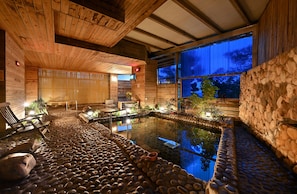 A wooden interior with a stone-lined pool, wooden benches, and a view of the outside. - CT Green Bay Hot-Spring Hotel (New Taipei City)