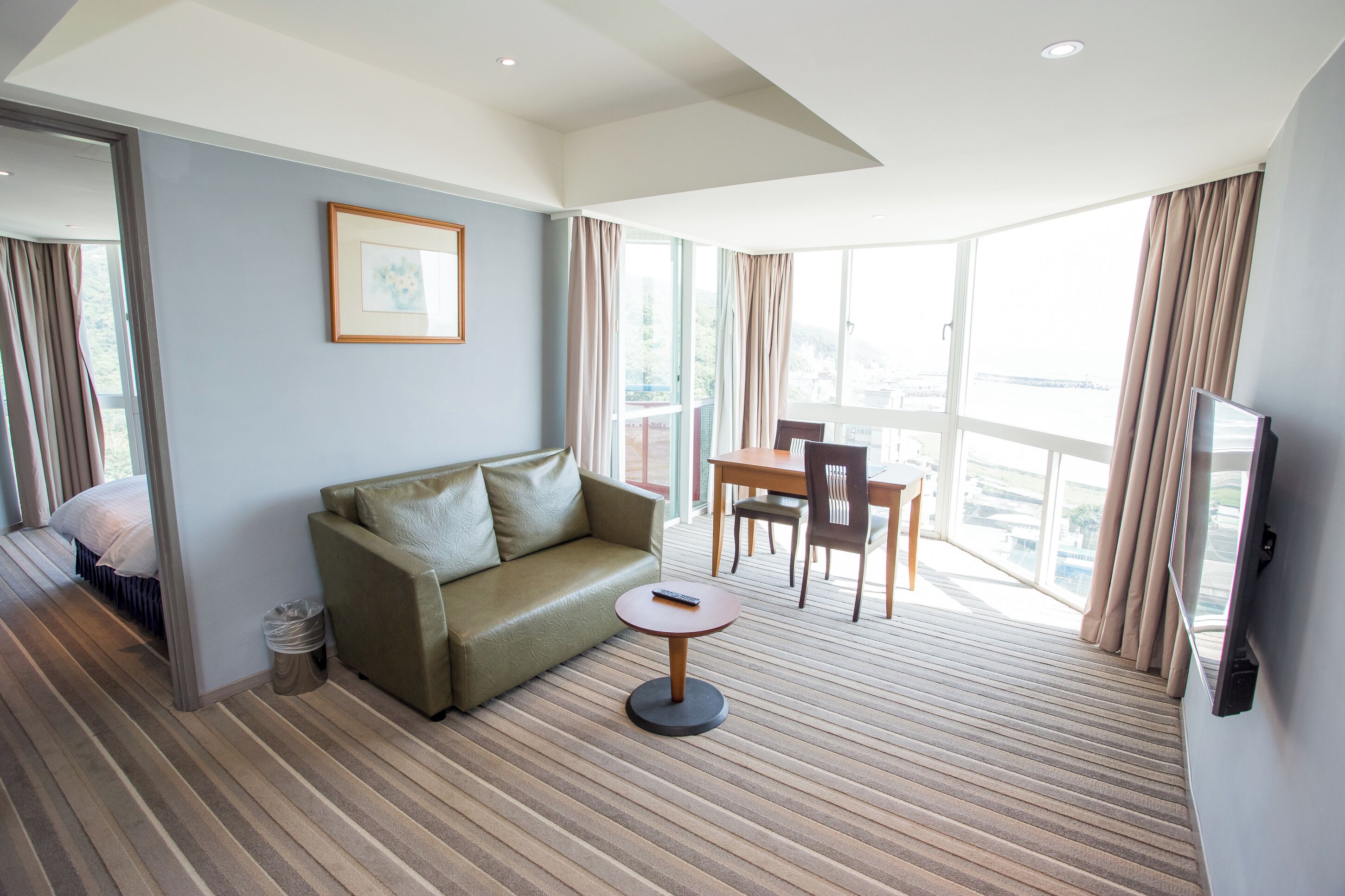 Ein Hotelzimmer mit einer Couch, einem kleinen Tisch, einem Fernseher und einem Balkon mit Vorhängen.