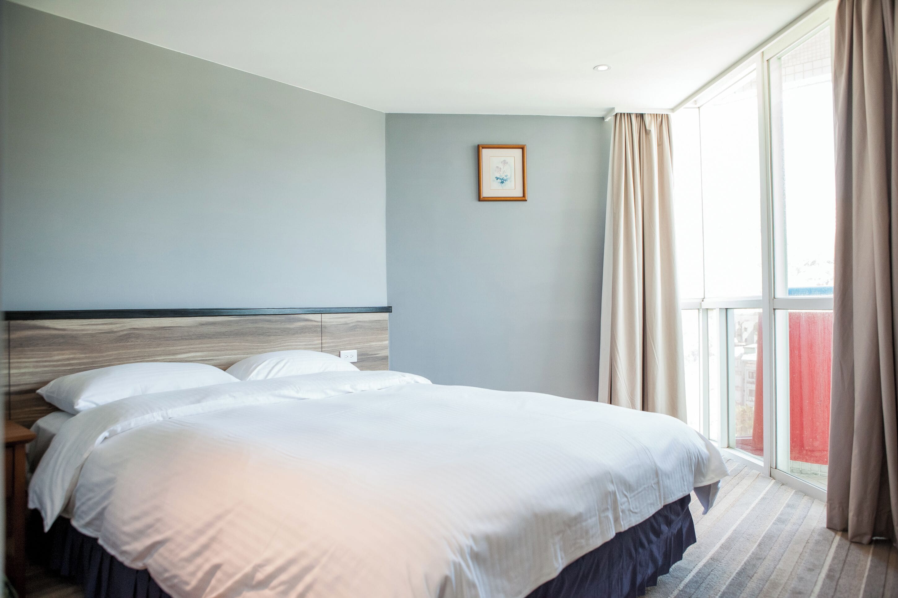 Una habitación de hotel con una cama grande, cabecera, ventana con cortinas e imagen enmarcada en la pared.