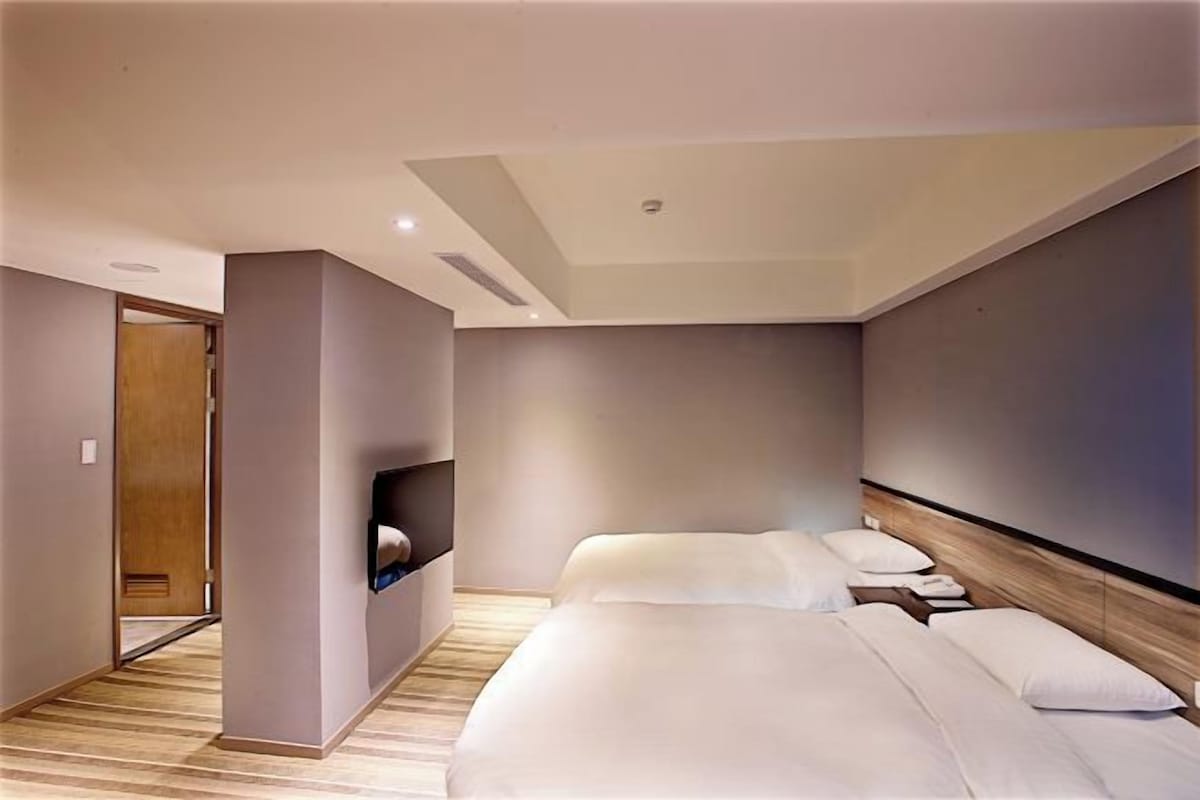 A modern hotel room with a large bed, a built-in TV, and a wooden floor.