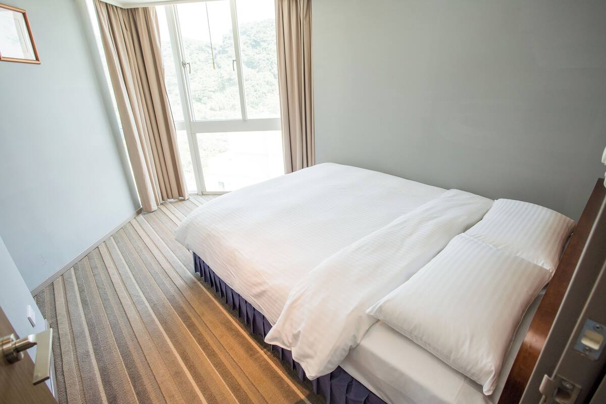 A hotel room with a large bed, a window with curtains, and a carpeted floor.