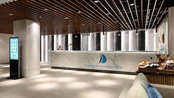 A hotel reception area with a marble counter, a digital menu board, and a wooden ceiling design.