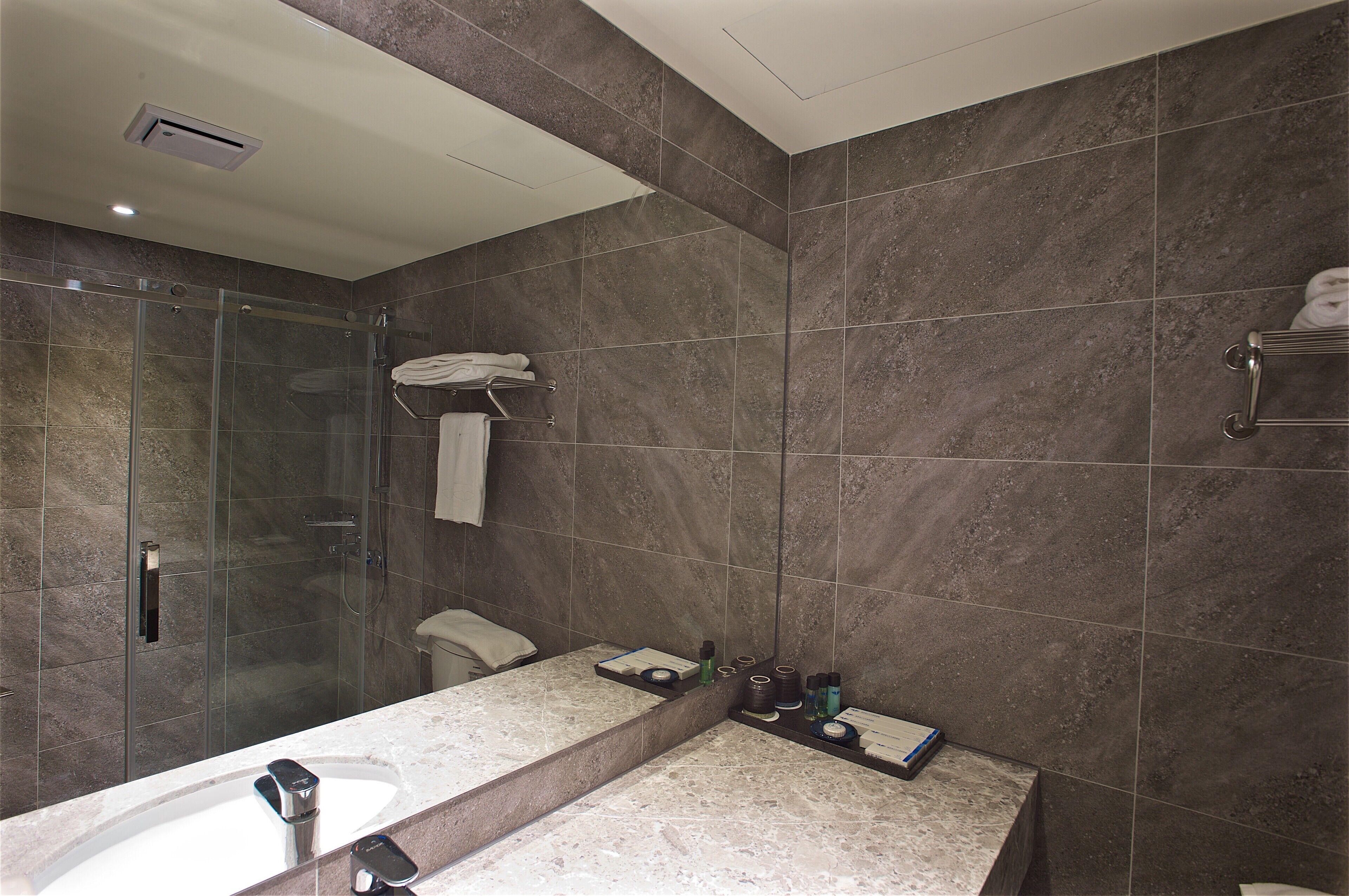 A modern bathroom with a glass shower enclosure, a marble sink, and a towel rack.