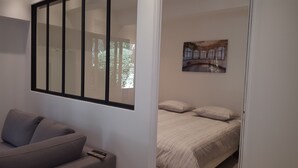 A bedroom with a bed, a sofa, a painting, and a window with blinds. - Apartments 2 bedrooms in garden floor in the heart THE MARAIS (Paris)