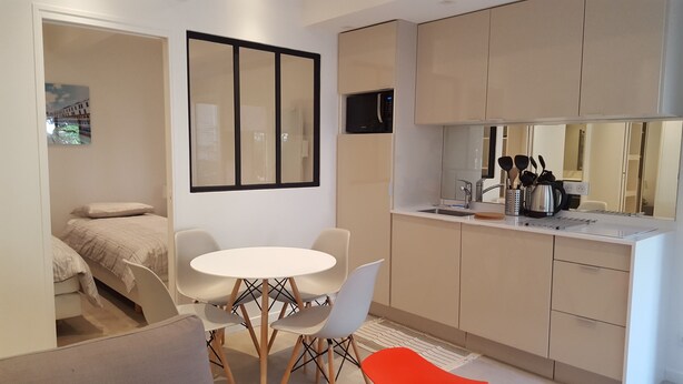 A compact hotel room with a kitchenette, a dining area with a round table and chairs, a bed with a headboard, and a large mirror. - Apartments 2 bedrooms in garden floor in the heart THE MARAIS (Paris)
