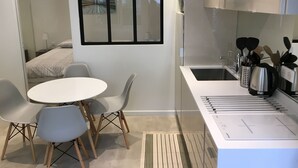 A modern kitchen with a white countertop, a sink, and a range hood. There are two chairs and a small table in the dining area. - Apartments 2 bedrooms in garden floor in the heart THE MARAIS (Paris)