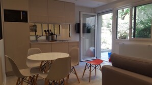 A modern kitchen with a microwave, a sink, and a dining area with chairs and a table. There is a sliding glass door leading to an outdoor area with a view of trees. - Apartments 2 bedrooms in garden floor in the heart THE MARAIS (Paris)