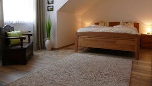 Una camera da letto con un letto di legno, un comodino con una lampada, una sedia, un'ampia finestra con tende e un vaso con piante verdi.
