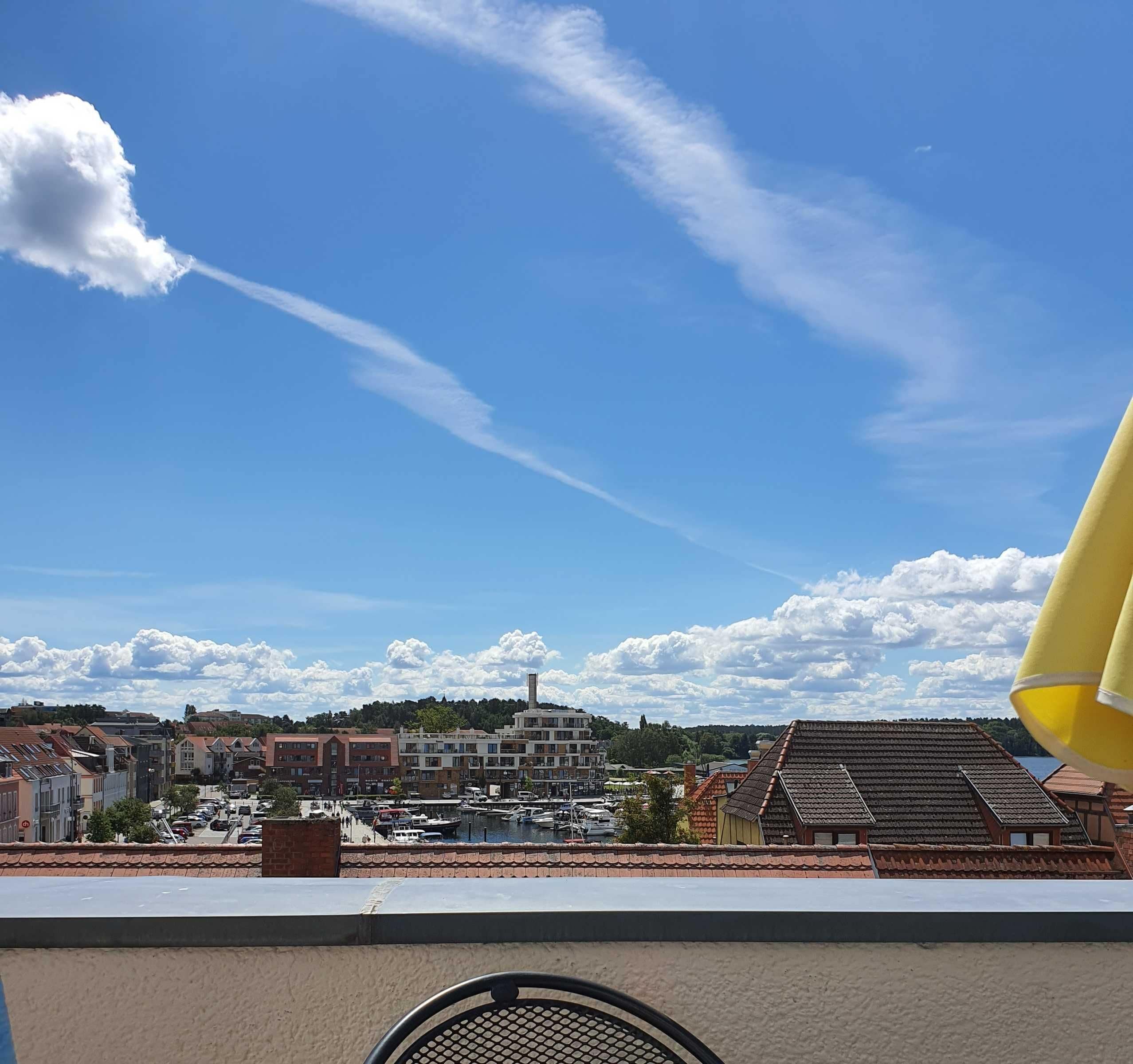 Eine Küstenstadt mit einem Yachthafen, Häusern mit roten Ziegeldächern und einem klaren, blauen Himmel mit Wolken.
