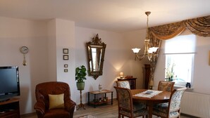 Un soggiorno con un divano in pelle marrone, un tavolo da pranzo in legno con sedie, una TV, una pianta in vaso, uno specchio e un lampadario.