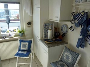 Uma cozinha com armários brancos, uma janela com vista e utensílios de cozinha com padrão azul e branco.