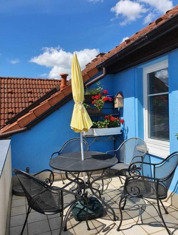 Uma casa azul com telhado de telhas, um guarda-chuva amarelo e uma mesa com cadeiras.