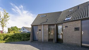 A building with a tiled roof, brick walls, and a paved entrance area. - Holiday house "White Shell" - large garden - parking lot directly at the house  (Brouwershaven)