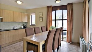 A modern kitchen with wooden cabinets, a dining table with six chairs, and a large window with curtains. - Holiday house "White Shell" - large garden - parking lot directly at the house  (Brouwershaven)